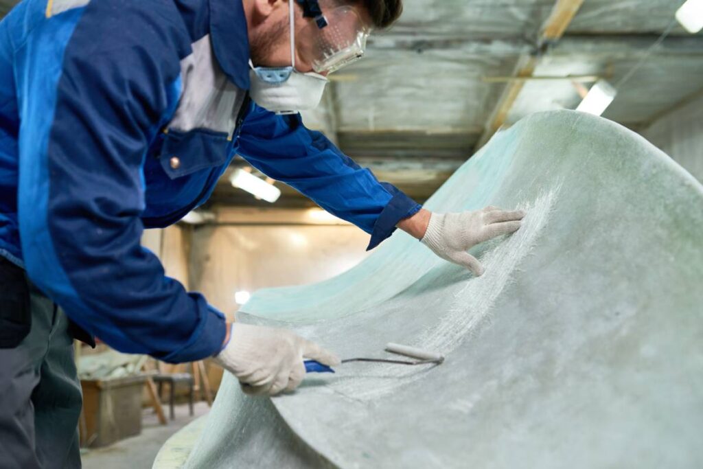 Unrecognizable mature man wearing protective mask repairing boat while working in yacht workshop, covering boat with pre-paint base coating,  copy space