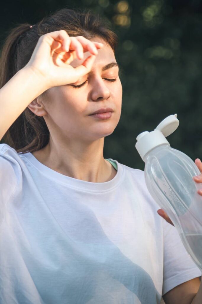 Attractive young woman drinks water after jogging in the park, training in nature.