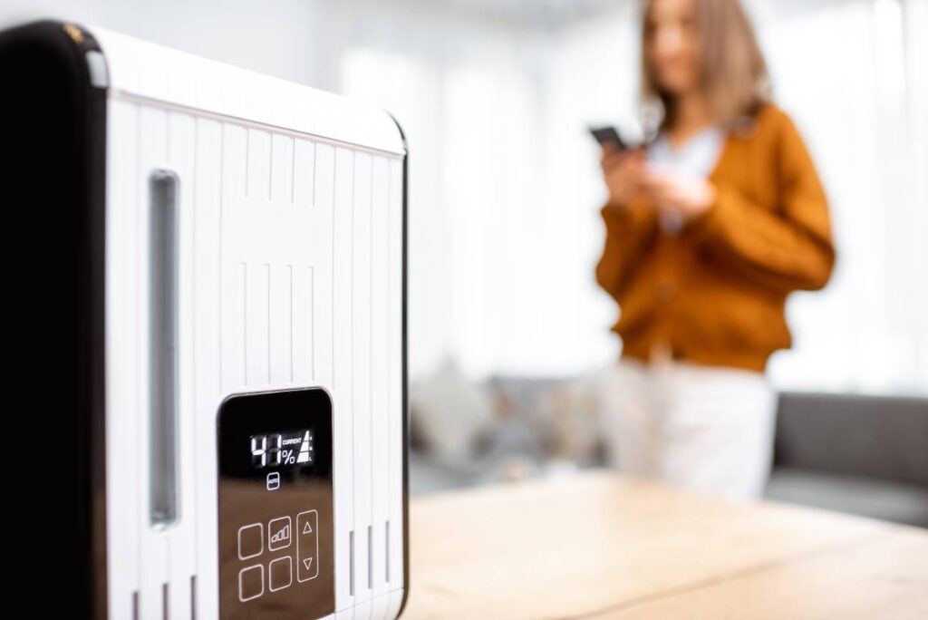 Close-up on a smart air humidifier with touch screen, woman controlling it with smart phone on the background