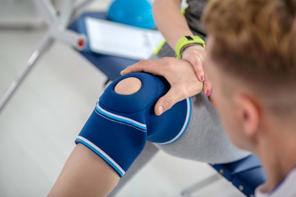 At rehabilitation center. Male physiotherapist hands examining knee bandage of female patient