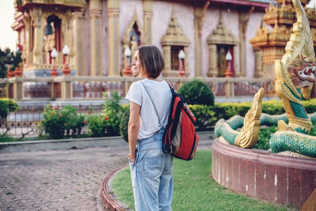 Woman backpacker seeing the sights Thai temple Wat Chalong on Phuket island. Travelling along. Girl carrying backpack. Tourism. Amazing Thailand.