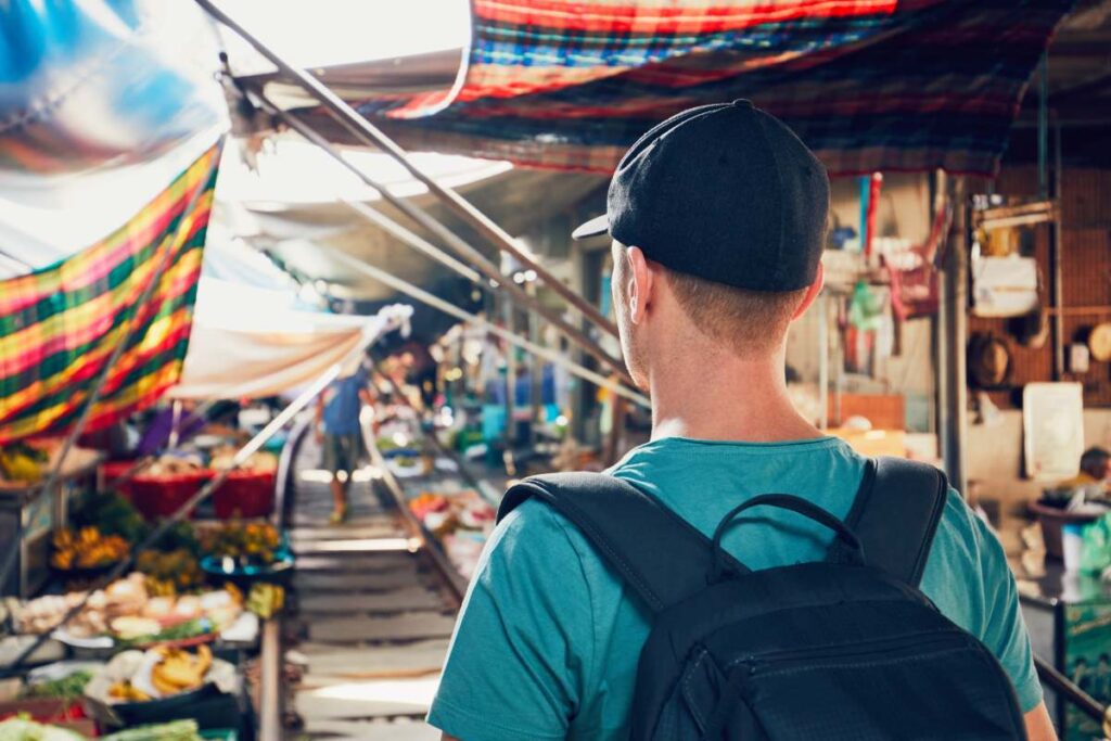 Young man (tourist) walking to open market along the railroad track. Maeklong railway market close to Bangkok in Thailand.