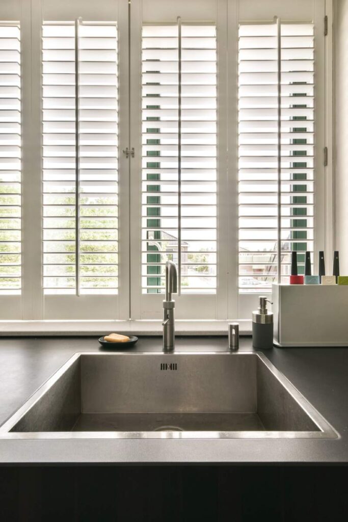 a kitchen sink and window with plantation shutters in the window behind it, which is open to let light into the room