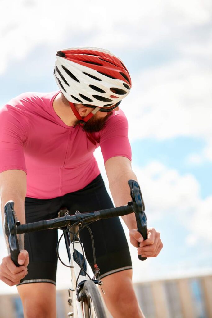 European bearded cyclist wearing helmet with pink t-shirt. Advise people to protection, blue sky on the background.