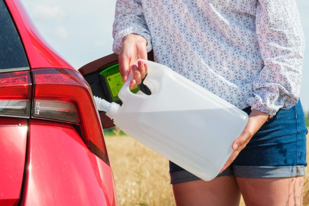 Close up woman refilling the red car with fuel or a diesel engine fluid from canister in the field, September 2021, Georgia, USA.